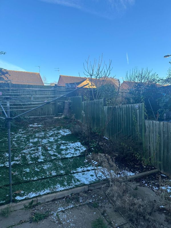 Snow-dusted back garden with an artificial lawn, rotary washing line and a freshly cut stump beside the fence