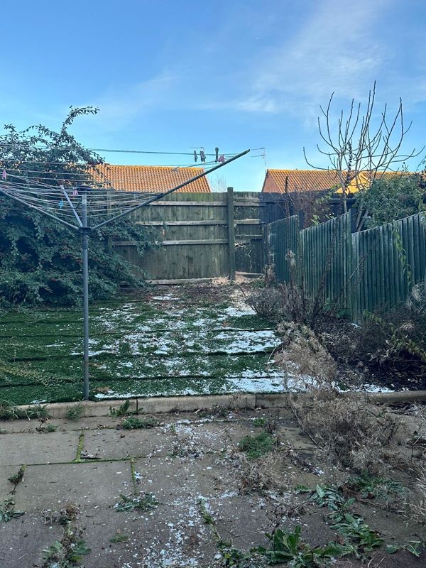 Back garden with patchy snow, a rotary washing line and cleared plant material lying near the paving
