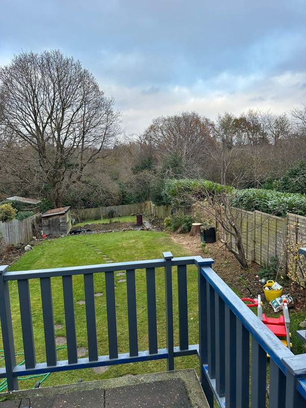 View over a blue balcony rail to a long lawn, a shed and tall bare trees behind the garden
