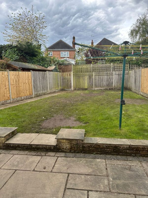 Open back garden with patchy lawn, new close-board fencing, rotary washing line and a sandstone-look patio