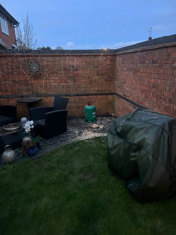 Garden corner with a low tree stump among slate chippings, patio chairs and a covered barbecue