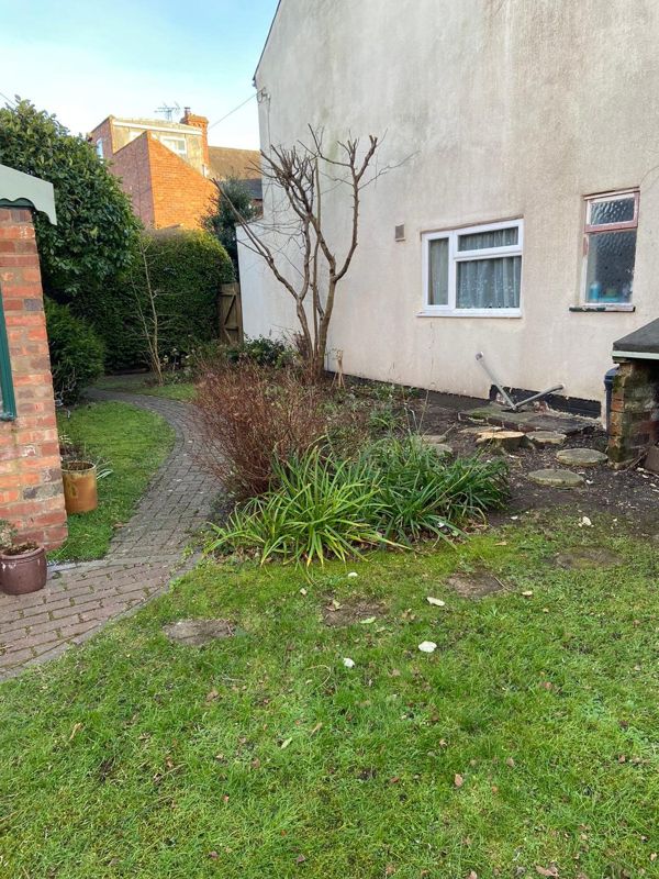 Cleared garden border beside a house showing a low stump, stepping stones and a bare stem