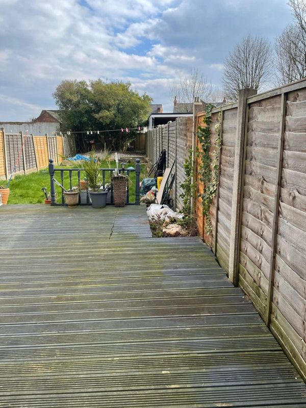Wooden decking beside a tall fence with ivy, leading to a lawn and a tree at the far end