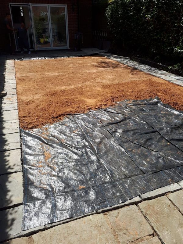 Orange sand laid over black membrane on a prepared garden area between paved edges