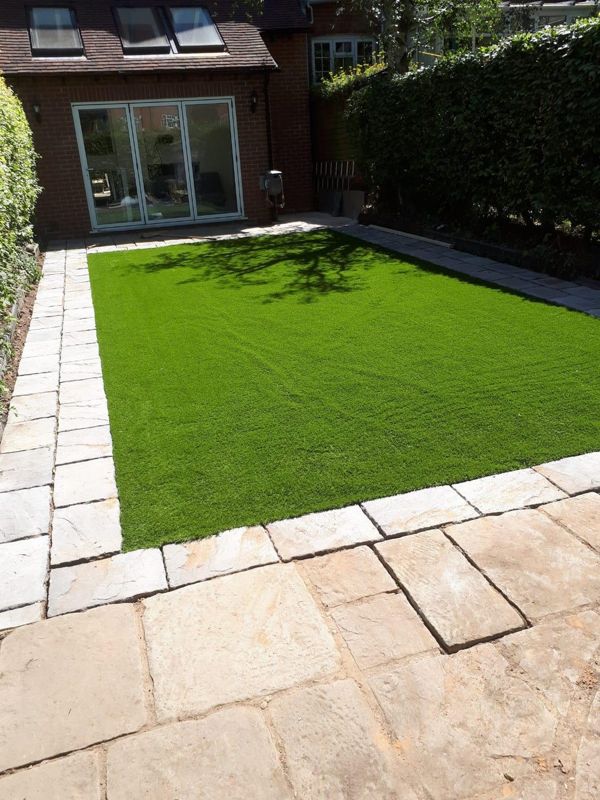 Finished green artificial lawn with paved border and large patio slabs in the foreground