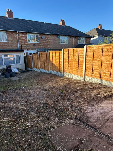 New orange-brown lapped fence panels on concrete posts beside bare soil in a terraced house garden