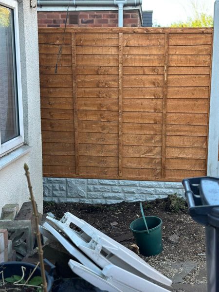 Short section of new fence panel against a house wall with stone-effect gravel board at the base