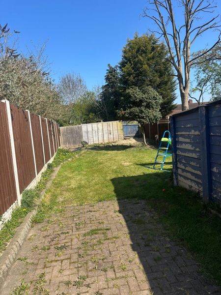 Back garden with block paving, mown lawn and fences on both sides leading to tall trees