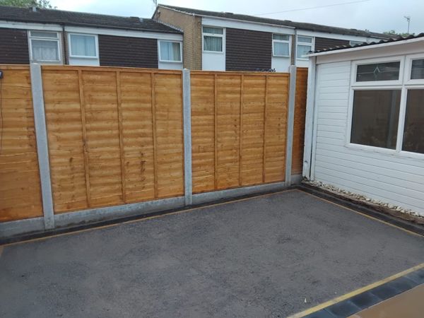 New lapped fence panels on concrete posts above a compacted grey stone base in a small garden