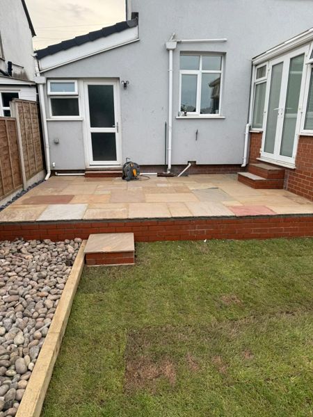 Raised paved patio with a red brick front beside a pebble border and a newly laid lawn