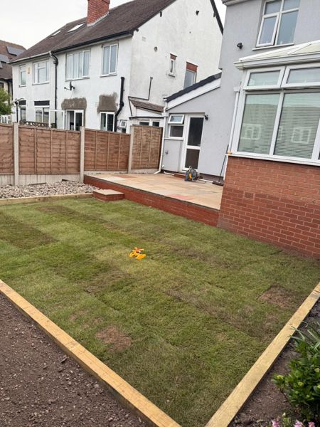 Freshly rolled turf with timber edging in front of a raised patio and a brick bay extension