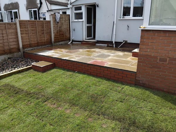 Raised patio with brick front and a pebble border beside a new lawn, seen from the side