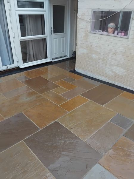 Close view of orange and brown sandstone-look slabs laid with dark edging beside a white brick wall