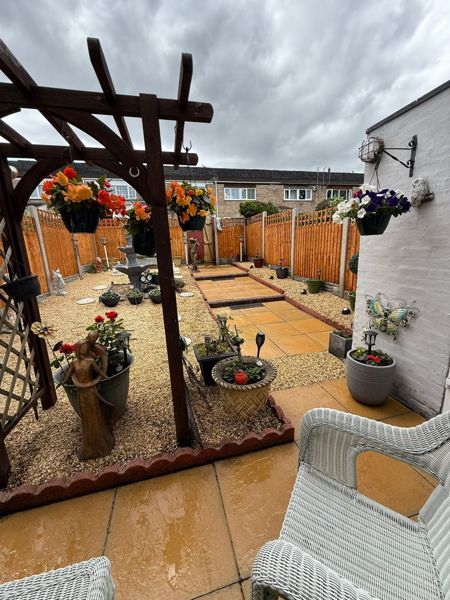 Small garden through a wooden pergola with hanging baskets, gravel, stepping stones and new fencing at the far end