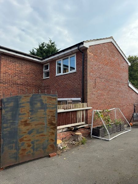 Brick gable wall and old fence after the conifers were removed, with two short stumps visible