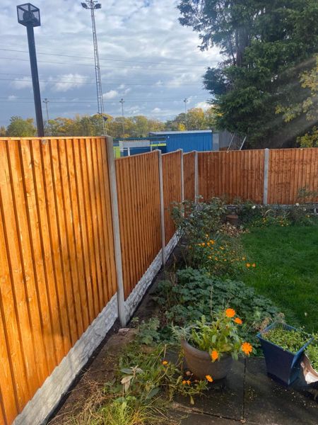 Orange-brown close-board fence between concrete posts above concrete gravel boards, with flowers in front