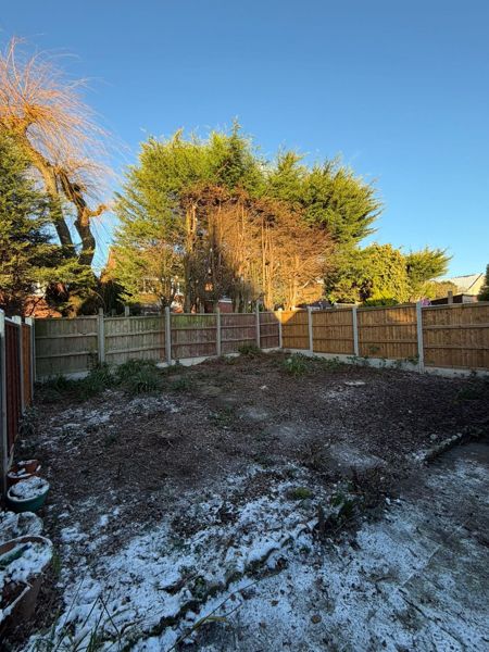 Cleared garden seen from the patio with frost on the ground and a bare-topped tree to the left of the fence