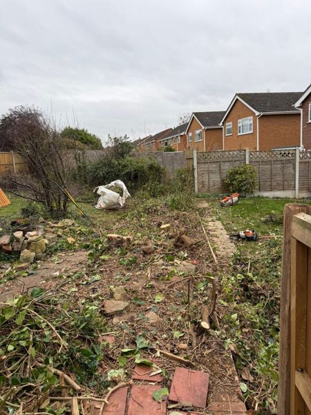 Cleared garden border strewn with cuttings and a white waste bag beside an old fence post