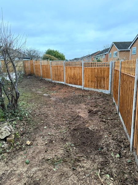 Finished brown close-board fence with trellis top and concrete gravel boards beside cleared soil