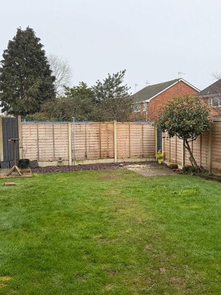 Back garden lawn with a slate chipping border and fence, with a low stump and no tree