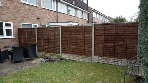 New brown overlap fence panels on concrete posts and gravel boards beside a patio and lawn
