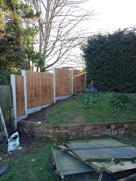New close-board fence panels between concrete posts with old green panels stacked on the lawn