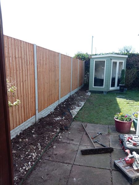 Long run of new close-board fencing beside a green summerhouse and paved patio area