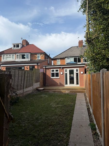Lawn, decking and a paved path behind a brick extension between fences