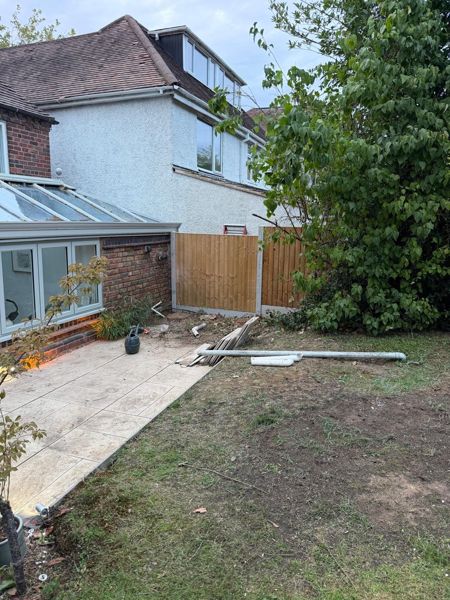 Cleared garden with bare lawn, paved patio, new close-board fence panels and a flat stump by the conservatory